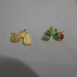 Peut inclure: Deux breloques en métal doré. L'une est en forme de chenille texturée. L'autre est une breloque chenille colorée avec des rayures vertes, bleues et noires, une tête rouge et une petite boucle pour suspendre.