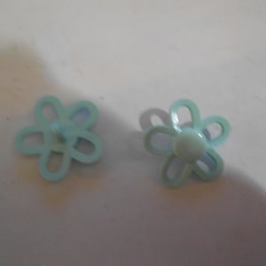 May include: Two light blue flower-shaped buttons. Each button has five petals and a rounded center. The buttons are made of plastic and are designed for sewing or crafting projects. They are set against a white background.
