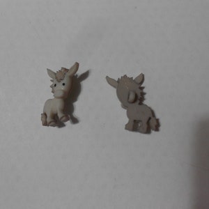 May include: Two plastic donkey figurines, one white and one gray, facing opposite directions. The white donkey is looking to the left, while the gray donkey is looking to the right.