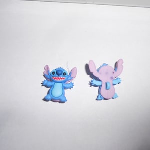 Puede incluir: Dos figuritas de Stitch, personaje azul y morado. La parte delantera de la figurita muestra a Stitch con un cuerpo azul y orejas moradas. La parte trasera de la figurita muestra a Stitch con un cuerpo morado y orejas azules.