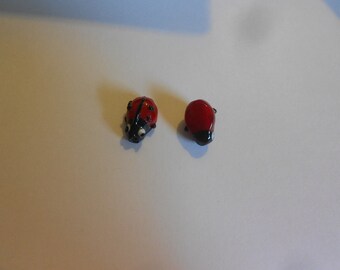 May include: Two small glass ladybug figurines. One ladybug is red with black spots and black legs. The other ladybug is red with a black underside.
