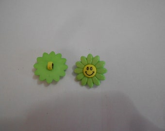 Op de afbeelding: Twee groene plastic bloemenknopen met gele centra. Een knoop heeft een smiley-gezicht.