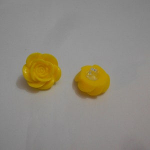 Puede incluir: Dos botones de plástico amarillo en forma de rosa. Un botón tiene un centro de plástico transparente.