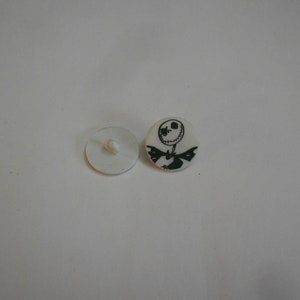 Puede incluir: Botón de plástico blanco con una imagen en blanco y negro de Jack Skellington de Pesadilla antes de Navidad.