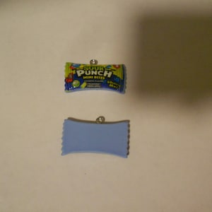 Può includere: Due ciondoli, uno blu e uno con un design di involucro di caramelle Sour Punch Mini Bites. Il ciondolo dell'involucro di caramelle ha il testo "Sour Punch Mini Bites" e "Fragola, anguria, mela verde, lampone blu".