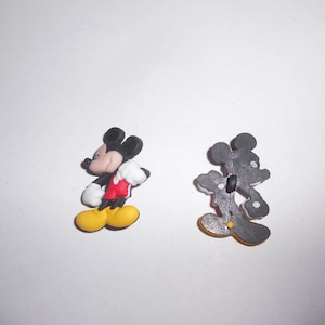 May include: Two Mickey Mouse-shaped buttons. One button shows Mickey Mouse in a side view, with black ears, a red jacket, white gloves, and yellow shoes. The other button shows the back of Mickey Mouse.