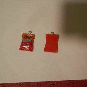 May include: Two small charms, one shaped like a bag of Cheetos with the text "Cheetos Puffy" and the other a solid red rectangle.