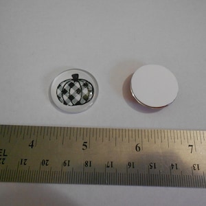 Könnte beinhalten: Ein klarer, runder Magnet mit einem schwarz-weiß karierten Kürbisdesign. Ein zweiter, leerer weißer Magnet ist ebenfalls sichtbar. Ein Metalllineal zeigt Messungen in Zentimetern.