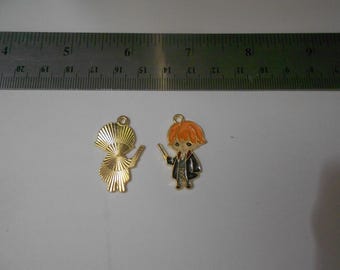 Op de afbeelding: Twee metalen bedels. Eén is een goudkleurige bedel van een persoon met een toverstaf. De andere is een bedel van een persoon met oranje haar, een toverstaf en een zwarte jas. Een liniaal staat op de achtergrond.