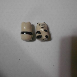 May include: Two small, ceramic chopstick rests. One is a cream color with a black stripe, and the other is a panda bear design with black spots and a smiling face. These decorative rests are for Asian-style dining.