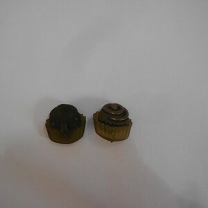 May include: Two small chocolate cupcake shaped ornaments. One is plain brown and the other has a swirl of brown icing on top.