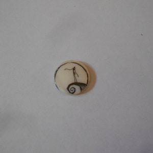 Può includere: Un bottone rotondo bianco con un'immagine in bianco e nero di Jack Skellington de The Nightmare Before Christmas in piedi su una collina.