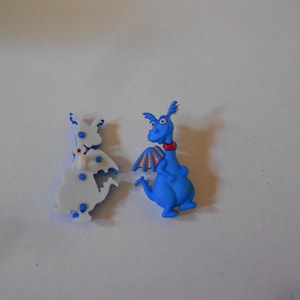 Könnte beinhalten: Zwei blaue Plastik-Drachenfiguren. Ein Drache blickt nach vorne mit ausgebreiteten Flügeln, während der andere Drache mit eingeklappten Flügeln nach hinten blickt. Beide Drachen haben einen roten Kragen.