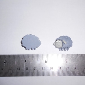 May include: Two small, light blue sheep figurines. One is a simple outline, the other has a face and legs. A metal ruler with inch markings is in the foreground.