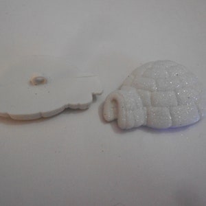 以下が含まれることがあります： イグルーの形をした白いプラスチックボタン2つ。1つのボタンは中央に穴があり、もう1つはキラキラと光る素材で覆われています。