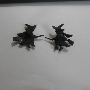 Puede incluir: Dos siluetas de bruja negras de plástico sobre un fondo blanco. Cada bruja vuela en una escoba con un sombrero puntiagudo y una larga capa fluida.