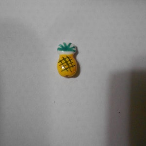 May include: A yellow ceramic pineapple charm with green leaves and brown lines.