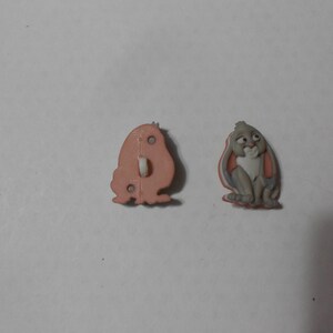 May include: Two plastic buttons featuring a cartoon rabbit. One button shows the rabbit's face, while the other shows the back of the button with a hole for sewing.