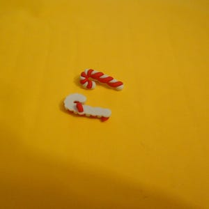 May include: Two red and white candy cane shaped ornaments on a yellow background.