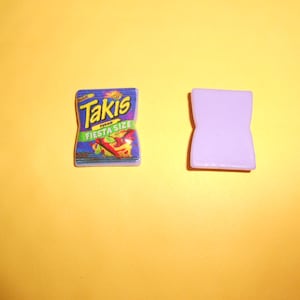 May include: A purple and blue plastic charm with the words "Takis Fuego Fiesta Size" on it.