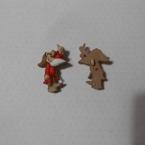 Könnte beinhalten: Ein Plastikknopf mit einer Cartoon-Darstellung eines Zwergs aus dem Disney-Film Schneewittchen und die sieben Zwerge. Der Zwerg trägt ein rotes und weißes Outfit und hat einen braunen Bart. Der Knopf ist an einer braunen Rückseite mit einem Loch zum Nähen befestigt.
