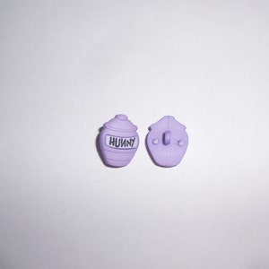 以下が含まれることがあります： ハチミツの壺の形をした紫色のプラスチックボタンが2つ。1つのボタンには「Hunny」と印刷されています。