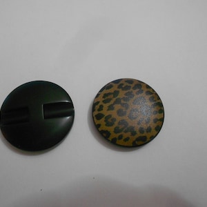 Puede incluir: Dos botones redondos. Uno es negro con una ranura horizontal. El otro es marrón con estampado de leopardo.