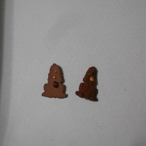 Puede incluir: Dos figuritas de perro de madera marrón. El perro de la izquierda está de pie sobre sus patas traseras con las patas delanteras levantadas. El perro de la derecha está sentado con las patas delanteras metidas debajo de su cuerpo. Ambos perros tienen pelo marrón y narices naranjas.