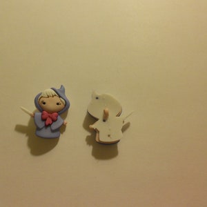May include: Two small, hand-painted figurines. One is a purple fairy with a pink bow and a white wand. The other is a white figure with a simple design.
