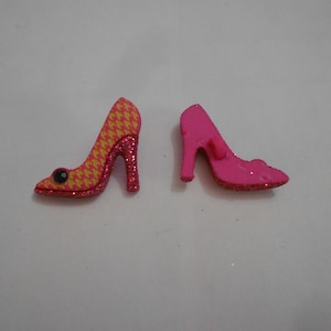 Peut inclure: Deux chaussures à talons hauts roses avec des paillettes. Une chaussure a un motif jaune et rose.