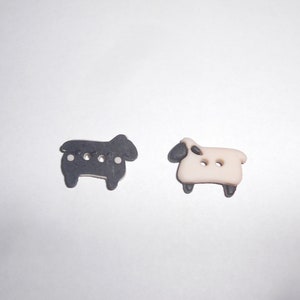 Puede incluir: Dos botones de plástico con forma de oveja, uno negro y otro blanco, con caras y patas negras.