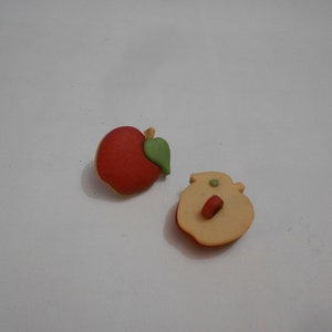 May include: Two apple-shaped buttons, one red and one yellow, with green leaves. One button has a hole in the centre.