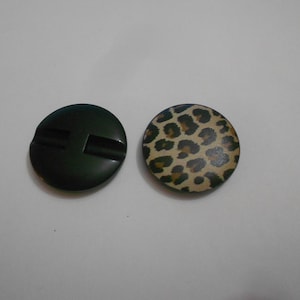 Könnte beinhalten: Zwei runde Knöpfe, einer schwarz mit einer Rille und einer mit einem braunen und schwarzen Leopardenmuster.