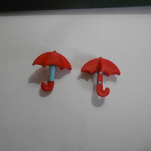 May include: Two red plastic toy umbrellas with blue handles. The umbrellas are about 2 inches tall.