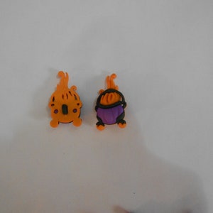 May include: Two Halloween-themed cauldron charms, one orange and one purple, with black accents and a flame design.
