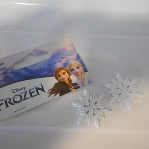 May include: A package of white snowflake buttons with a Disney Frozen logo and images of Elsa and Anna. The package says "Buttons, Boutons, Botones".