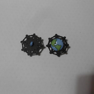 May include: Two black metal buttons with a geometric design. One button has a blue centre and the other has a green and blue globe design.
