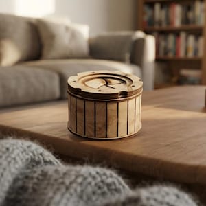 Könnte beinhalten: Eine zylindrische Holzbox mit hellbrauner Maserung und vertikalen Lamellen an den Seiten. Der obere Deckel ist kreisförmig und verfügt über einen mechanischen Iris-Öffnungsmechanismus in der Mitte, der mit kleinen Schrauben am Rand befestigt ist.