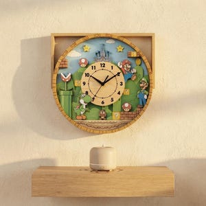 Può includere: Un orologio da parete circolare in legno con una scena 3D multistrato ispirata alla serie di videogiochi Super Mario. Il quadrante è in legno chiaro con numeri e lancette neri, circondato da personaggi come Mario, Luigi e Yoshi.