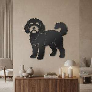 Op de afbeelding: Een zwart metalen wanddecoratie in de vorm van een pluizige hond met een gekrulde staart. Het silhouet is voorzien van gedetailleerde vachtstructuren en een lichtgekleurd gezicht, gemonteerd op een effen muur. De hond staat in zijaanzicht.
