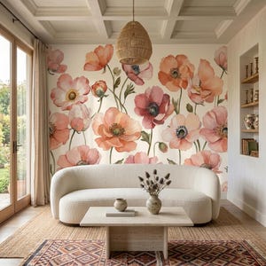 May include: A cream-colored curved sofa sits on a woven rug in front of a wall covered in floral wallpaper featuring large orange and pink poppies. A light-colored wooden coffee table holds a small vase with dried flowers and a ceramic bowl.
