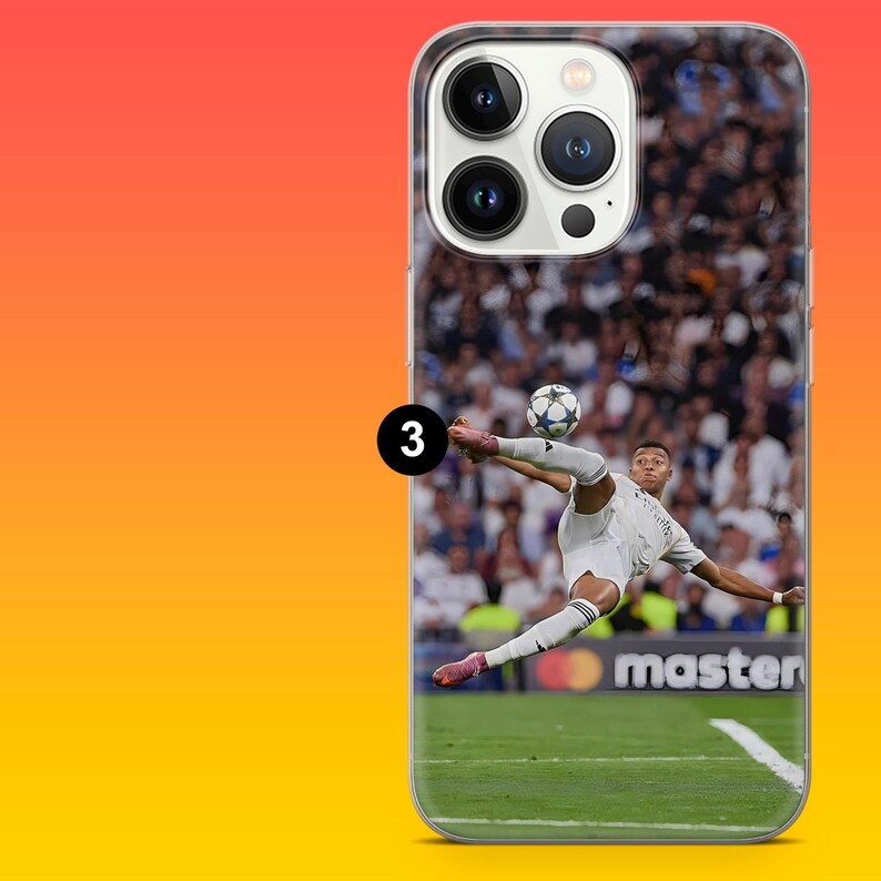 May include: A clear smartphone case featuring a printed graphic of a football player in a white kit performing a bicycle kick on a green pitch. The image includes a football in mid-air and a blurred stadium crowd background with the text master.