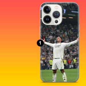 Puede incluir: Una funda transparente para smartphone con un gr&aacute;fico impreso de un futbolista con camiseta blanca y el texto Emirates Fly Better, de pie en un campo verde con los brazos extendidos frente a un fondo borroso de p&uacute;blico en el estadio.