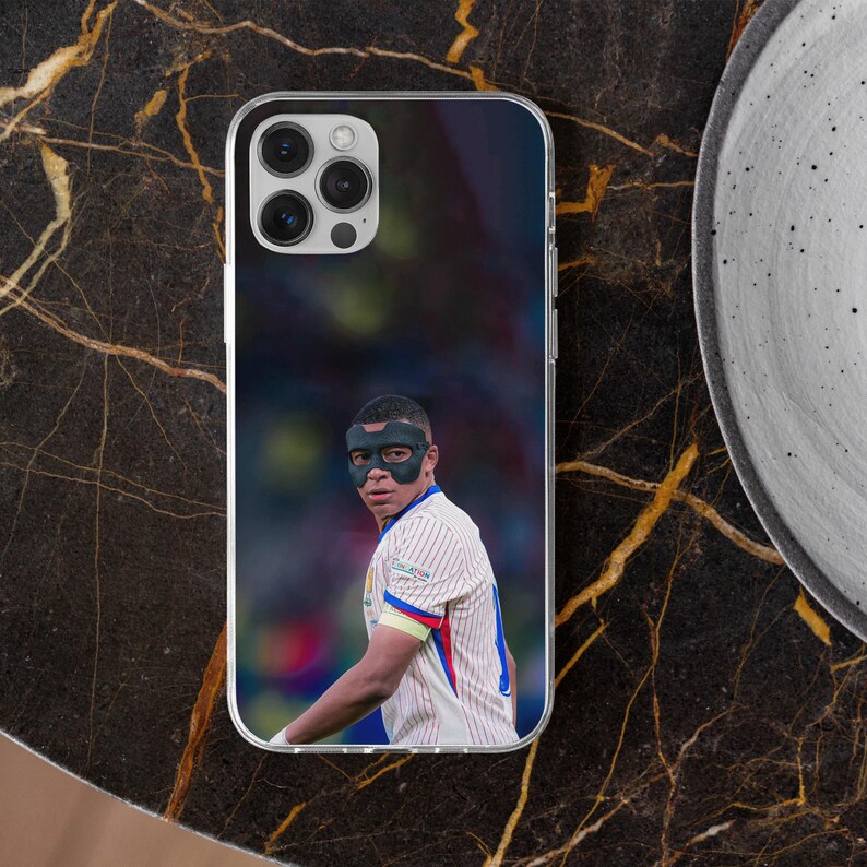 May include: A clear smartphone case featuring a printed image of a football player wearing a black protective face mask and a white jersey with thin red and blue vertical stripes. The player is shown from the chest up against a blurred background.