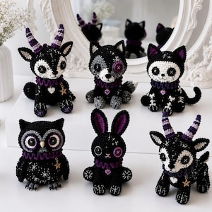 Può includere: Una collezione di sei figure all'uncinetto realizzate con filati neri, bianchi e viola. Il set comprende due creature con le corna, un lupo, un gatto con motivo a scheletro, un gufo e un coniglio, tutti decorati con occhi a bottone e ciondoli.