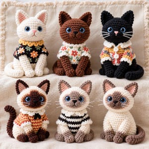 May include: Six crocheted cat figurines arranged in two rows. The top row features a white cat in a black floral sweater, a brown cat in a white floral sweater, and a black cat in a colorful patterned sweater. The bottom row shows three Siamese-style cats.