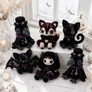 Può includere: Una collezione di sei peluche realizzati all'uncinetto a mano, tra cui due corvi neri con cilindro, una volpe bordeaux e crema, un gatto nero con dettagli viola, un pipistrello nero con ali decorate e una bambola con capelli in lana nera.