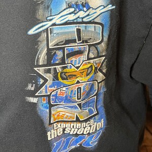 Może przedstawiać: Czarny t-shirt z nadrukiem graficznym zawierającym napis "Lary" u g&oacute;ry i "Experience the speed of Lite" u dołu. Wz&oacute;r zawiera duże białe logo "IROC" nałożone na niebieskawy obraz kierowcy wyścigowego w kasku i goglach ochronnych.