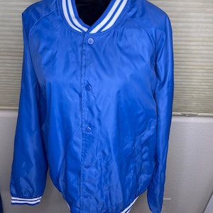 May include: A royal blue bomber jacket with a white and blue striped collar, cuffs, and hem. The jacket has a button-up front and two side pockets. The jacket is made of a shiny, lightweight material.