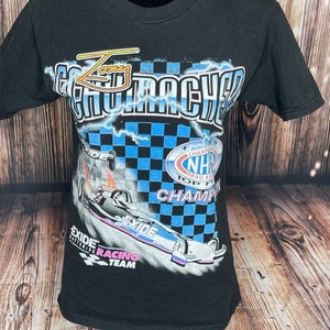 May include: Black t-shirt featuring a drag racing design. The graphic includes the words "Zany Go-Machers" and "Exide Batteries Racing Team". The design also features a race car, lightning bolts, and a checkered flag. The shirt has short sleeves and a crew neck.